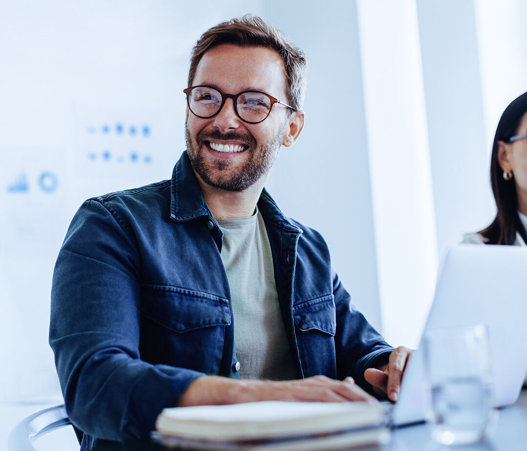 Bilde av smilende mann med laptop i et møte